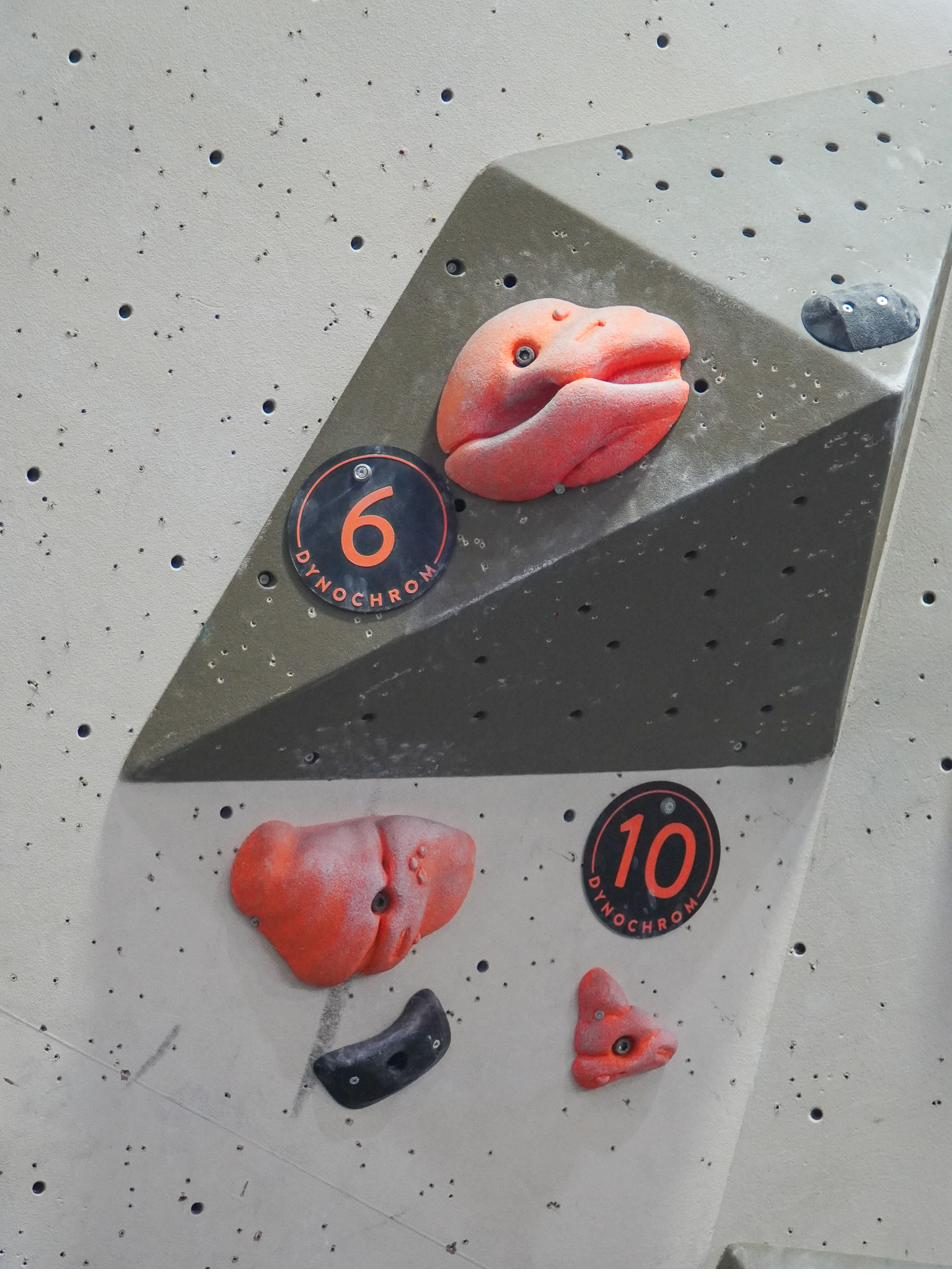 Boulderwand mit orangen Griffen und Routentags im Kundendesign