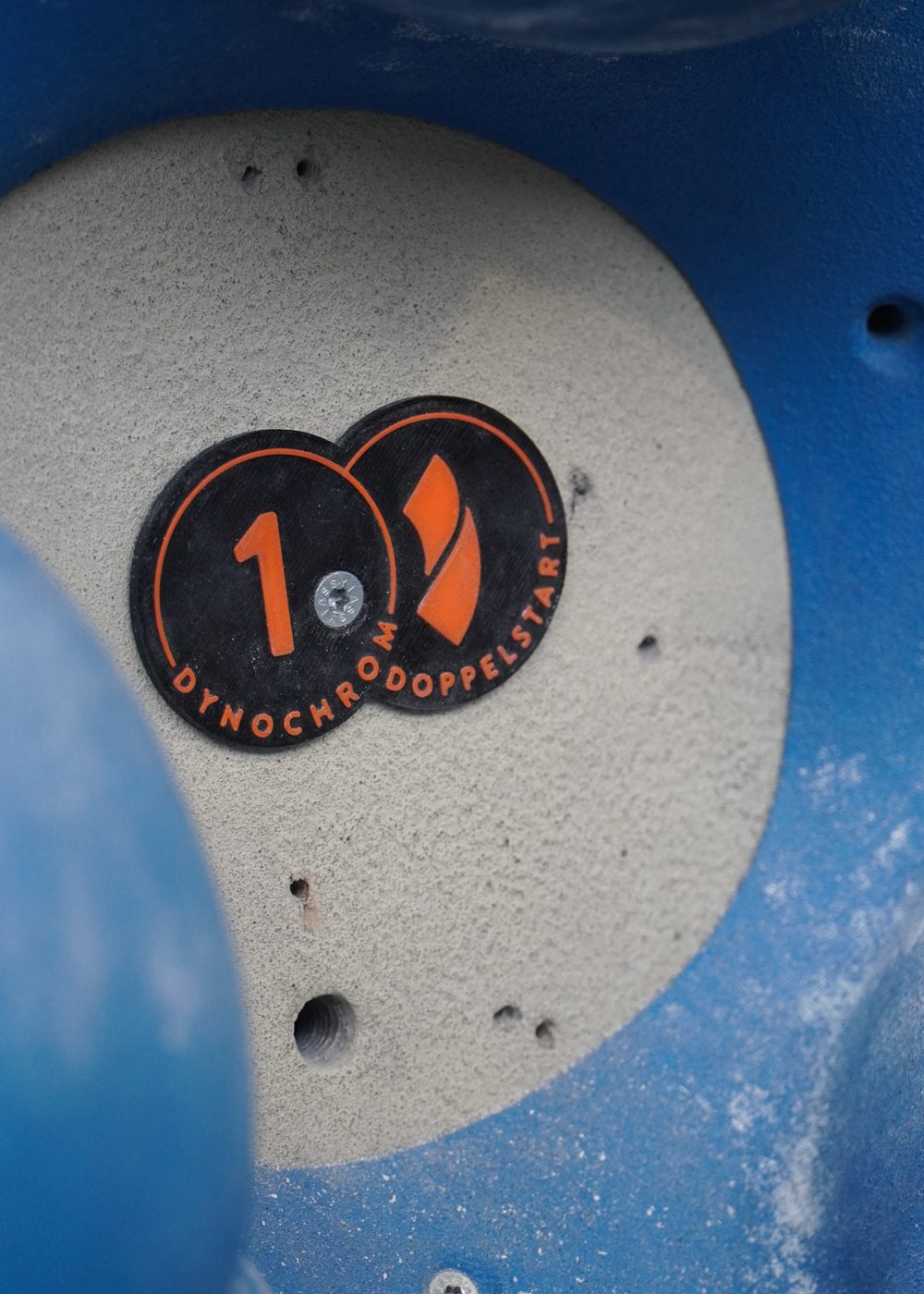 Spezial-Tag Doppelstart: zwei verbundene runde Tags mit Nummer und Logo an der Boulderwand